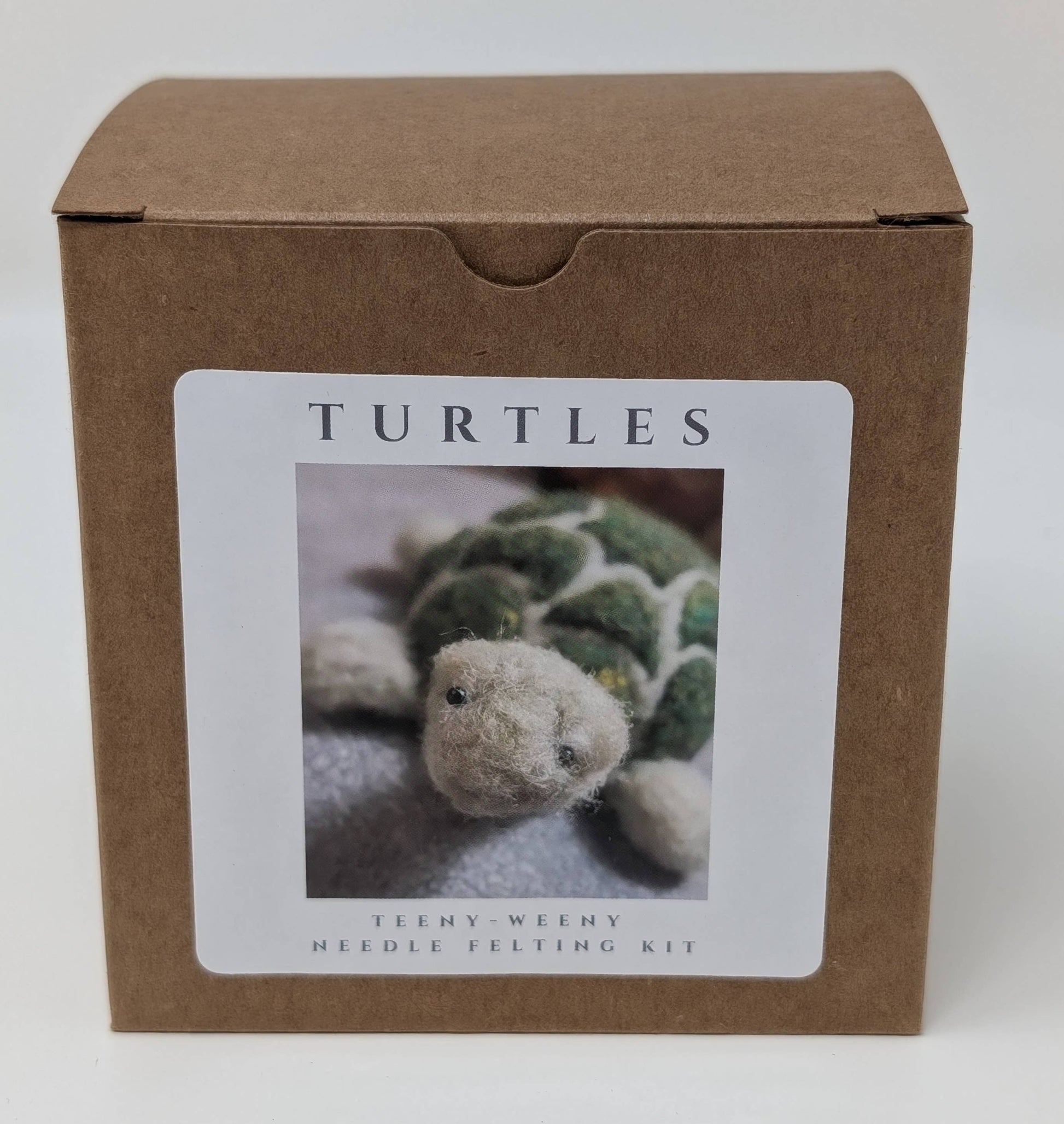 Brown cardboard box with a label featuring a needle felted turtle on a white background