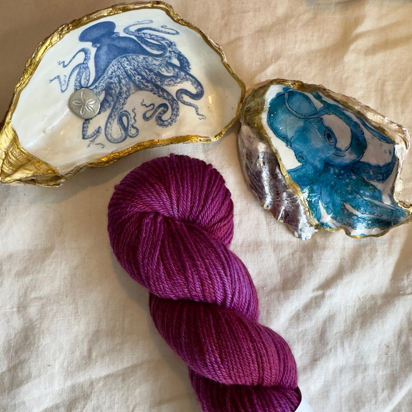 A hank of deep magenta-colored yarn next to two sea shells.