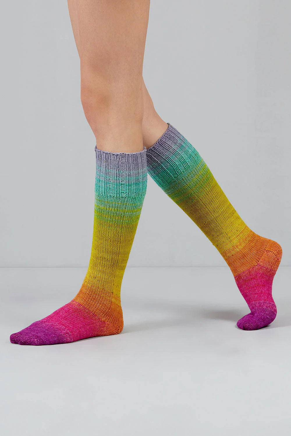 A pair of purple, pink, yellow, green, blue and grey gradient socks shown on feet against a white background