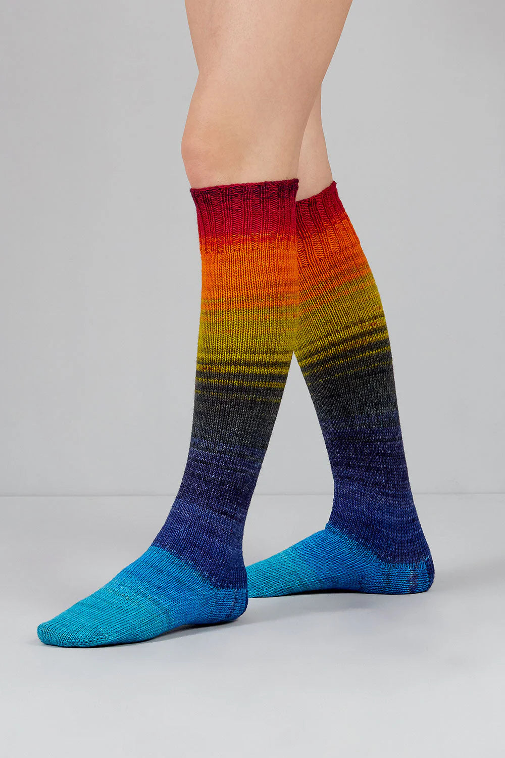 A pair of blues, grey, green, orange, and red gradient socks shown on feet against a white background