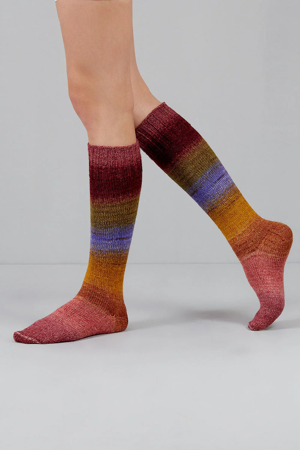 A pair of pink, orange, purple, brown, and red gradient socks shown on feet against a white background