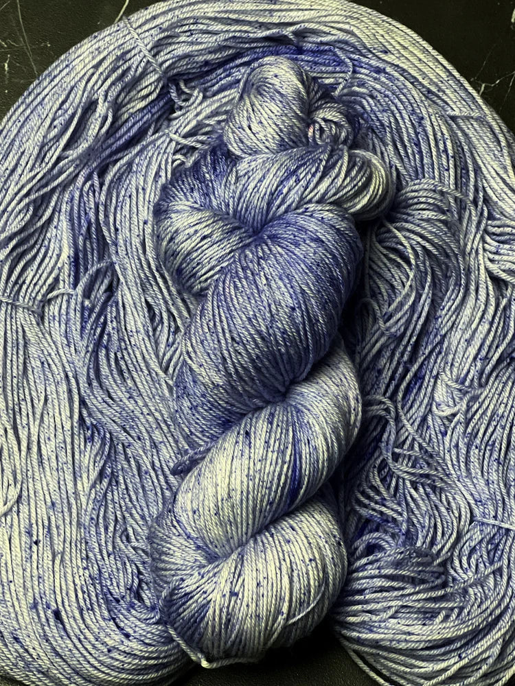 Gray and blue hank of yarn with speckles on a bed of gray yarn.
