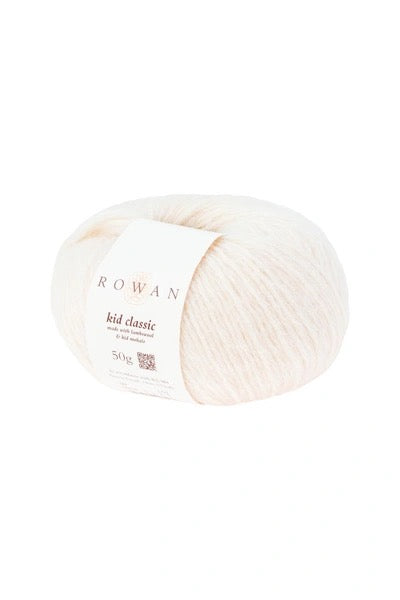 A ball of Rowan Kid Classic yarn in a soft off-white color, featuring a white paper label with the brand name 'ROWAN' and product details, set against a plain white background.