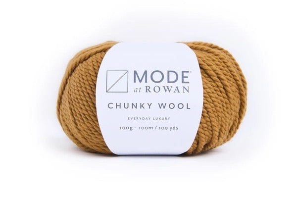 A golden color skein of Mode at Rowan Chunky Wool yarn in a warm camel brown color, wrapped with a white paper label, on a clean white background.
