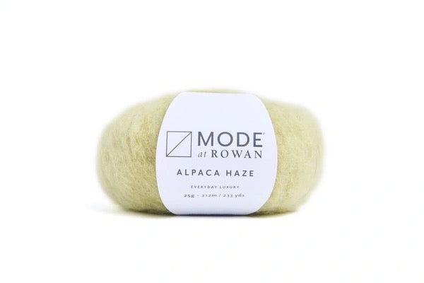 A single ball of Mode at Rowan Alpaca Haze yarn, shown on a clean white background. The yarn is a soft, pale cream-yellow color, and it has a white paper label wrapped around the center with black text and logo.
