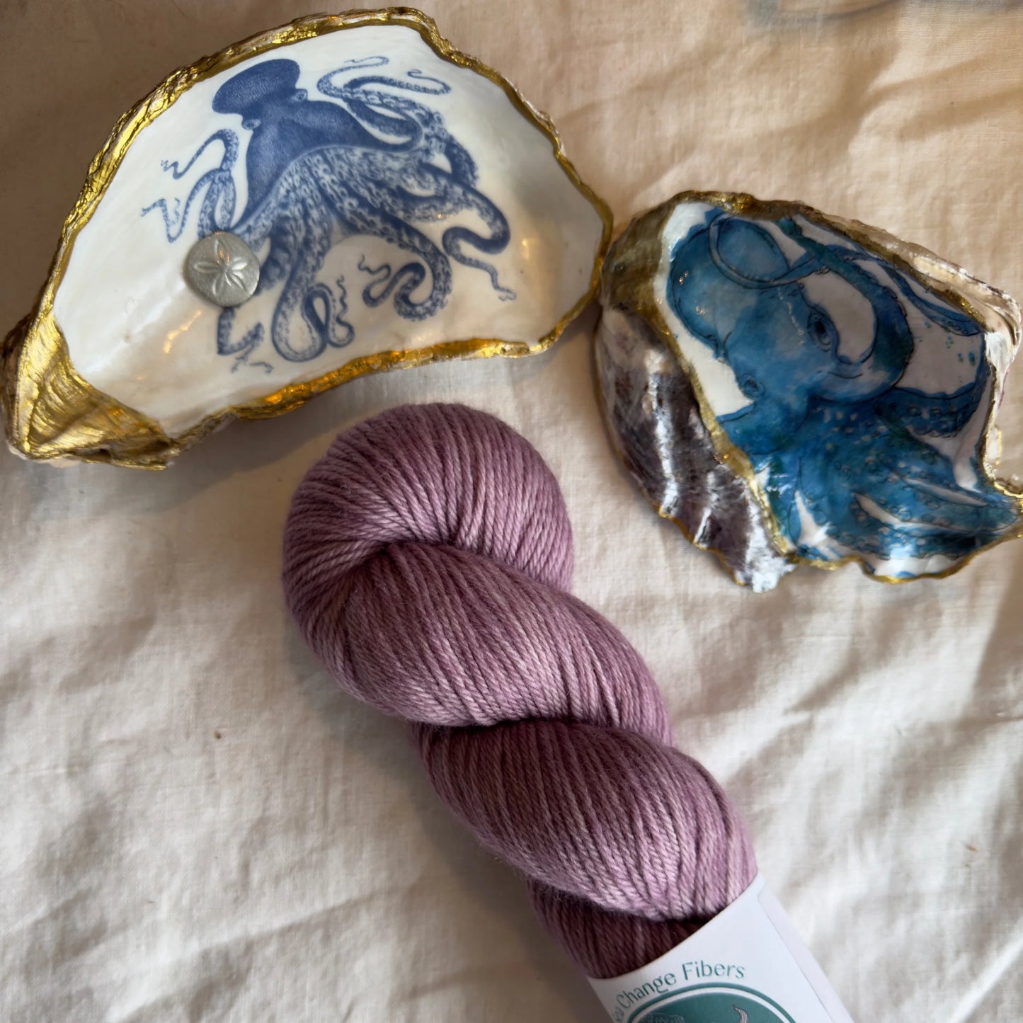 A hank of mauve-colored yarn next to two seashells.