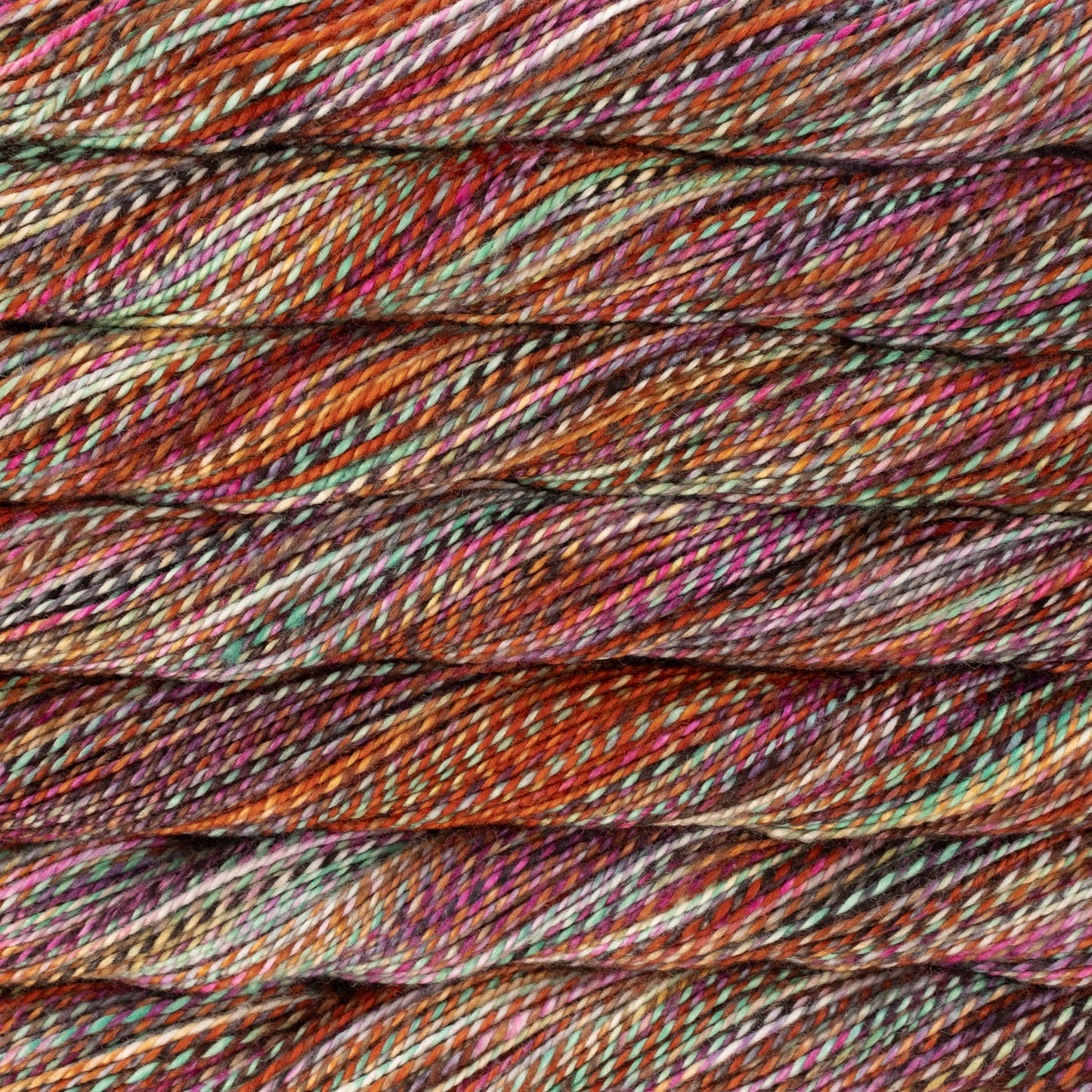 Close-up of twisted yarn strands in a variegated colorway of muted teal, sage green, tan, and brown and reds