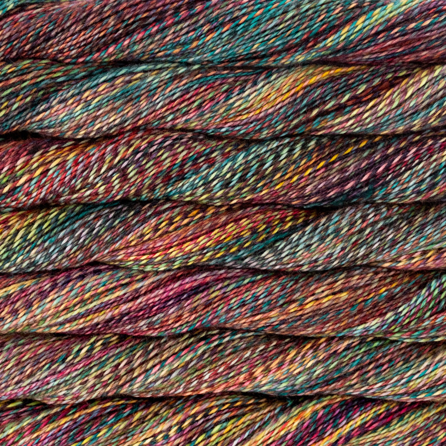 Close-up of folded variegated yarn twisted with a multicolor blend of teal, burgundy, pink, yellow, and orange threads.
