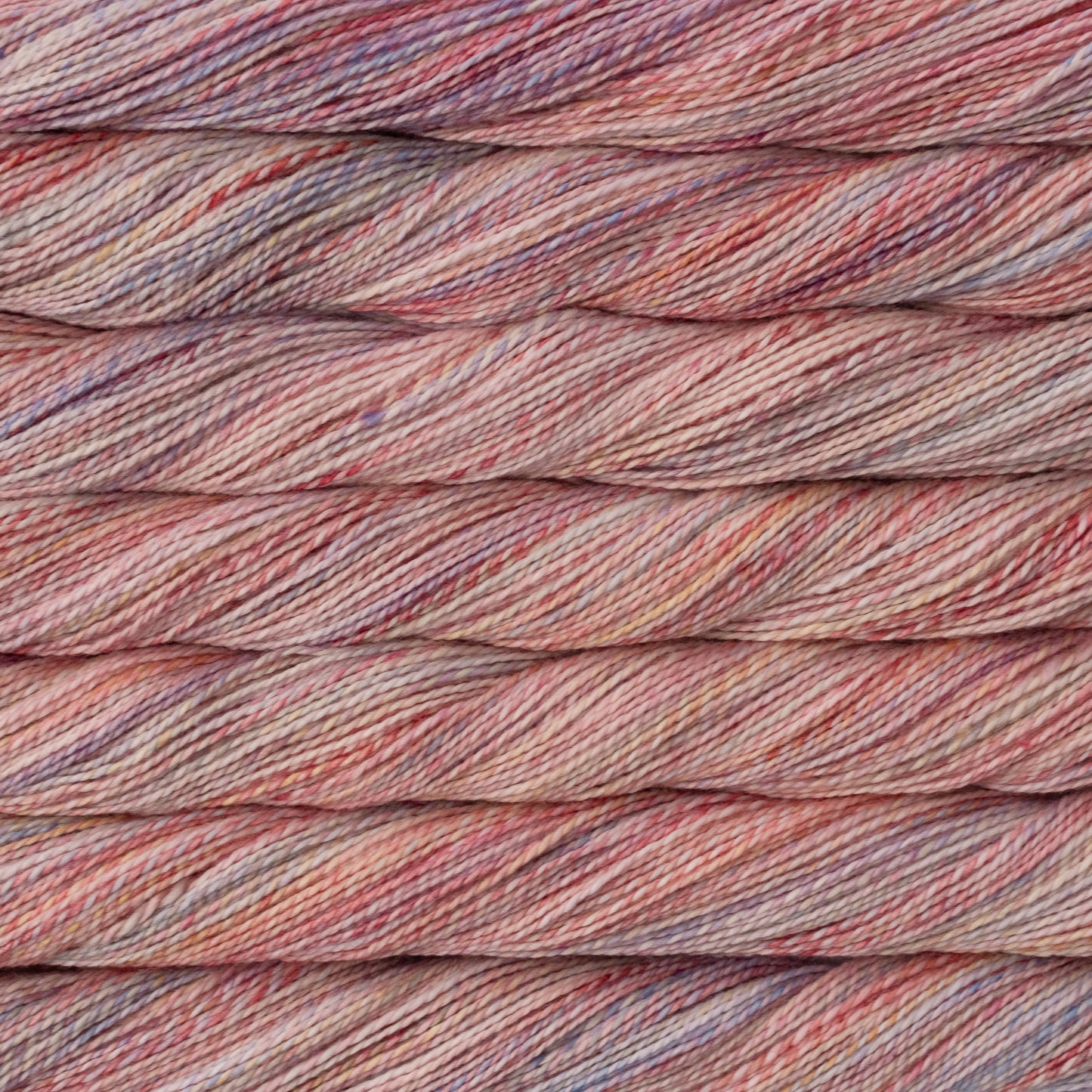 Close-up of Close-up of twisted yarn strands in a variegated colorway of muted pinks, purples, and various  pastels